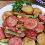 A white bowl with blue trim with a serving of sausage, green beans, and potatoes sheet pan meal in it with a title overlay at the top.