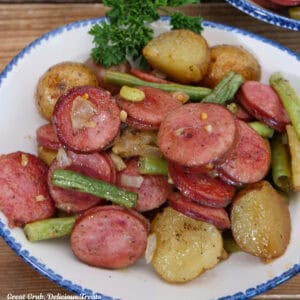 A white bowl with blue trim filled with a serving of sheet pan sausage green bean and potatoes.