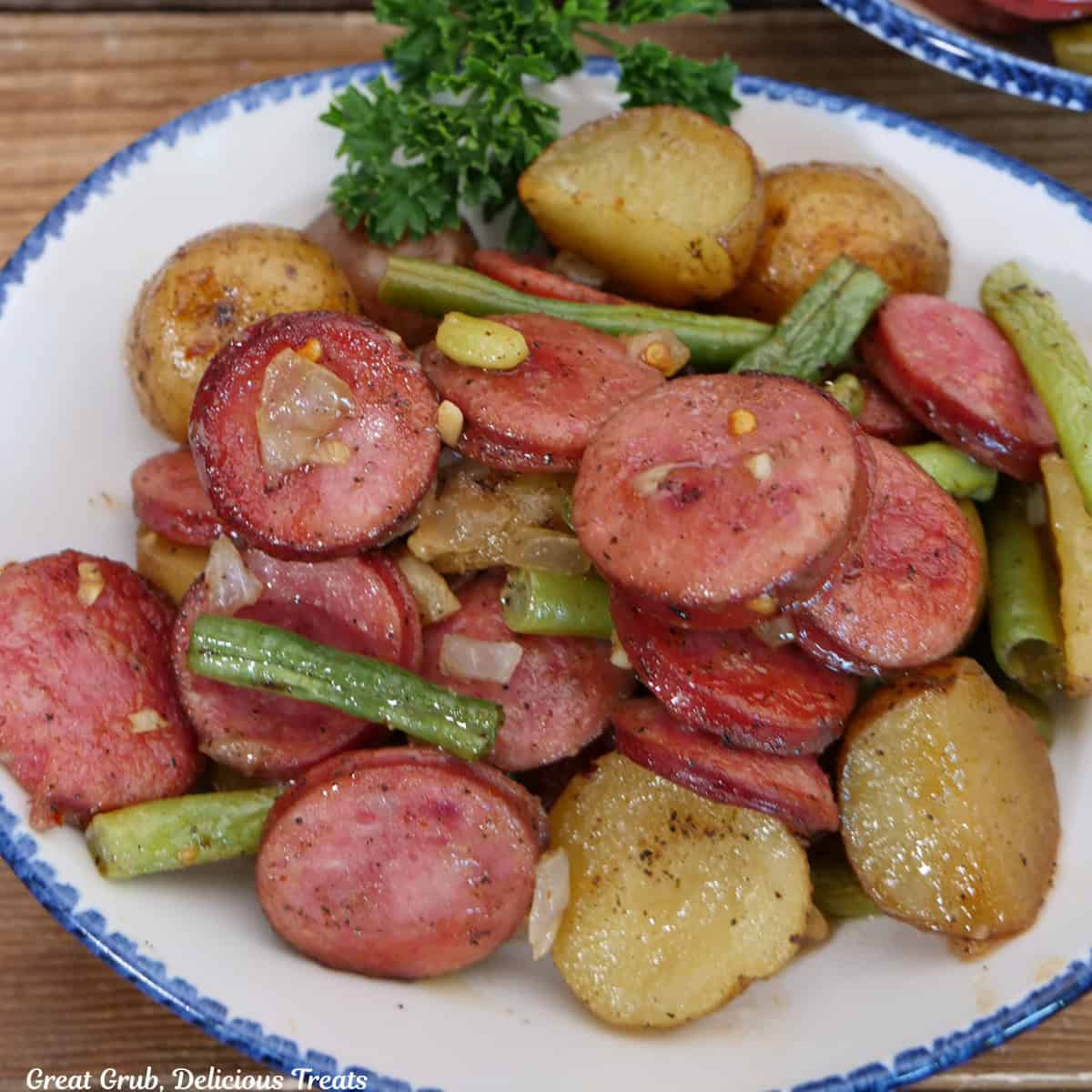 A white bowl with blue trim filled with a serving of sheet pan sausage green bean and potatoes.