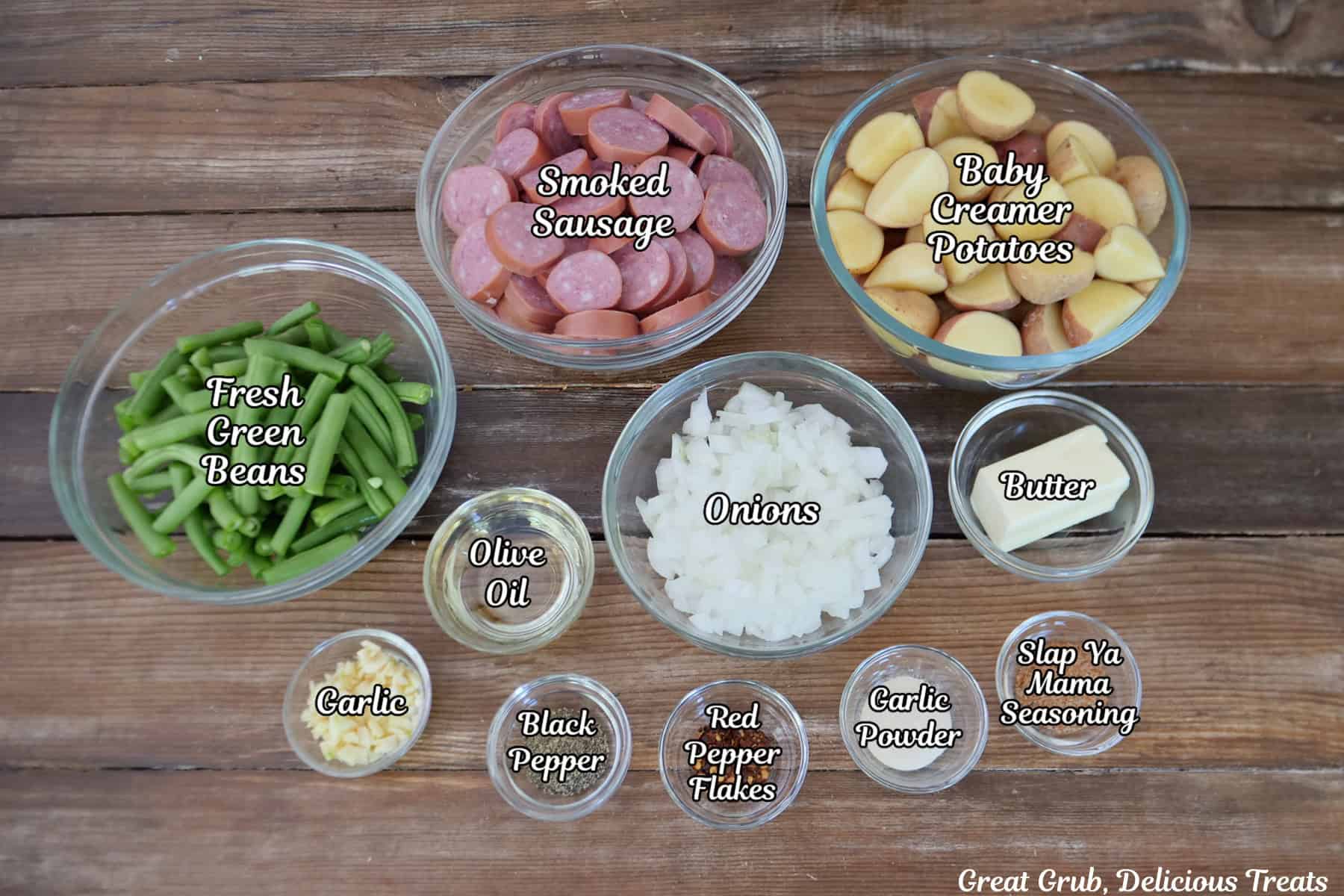 A rustic wood surface with all the ingredients placed on it to make sheet pan sausage green beans and potatoes.