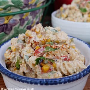 A white bowl with blue trim sitting on a wood surface with a serving of street corn pasta salad in it.
