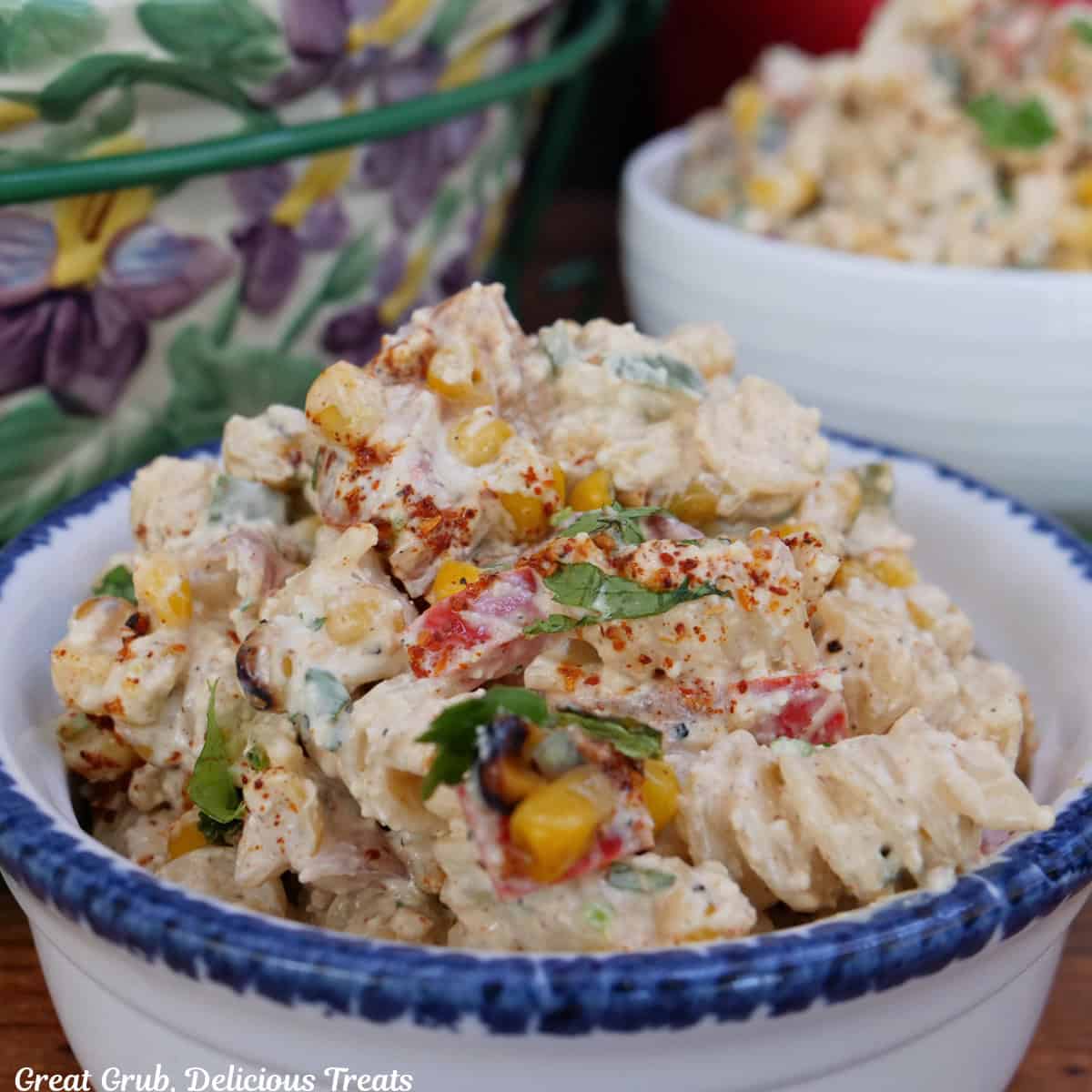 A white bowl with blue trim sitting on a wood surface with a serving of street corn pasta salad in it.
