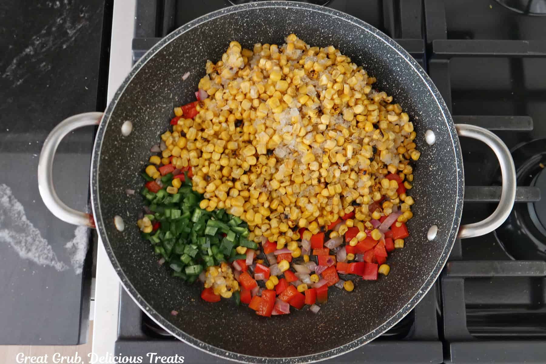 A frying pan with fire roasted corn, bell pepper, and onions in it.