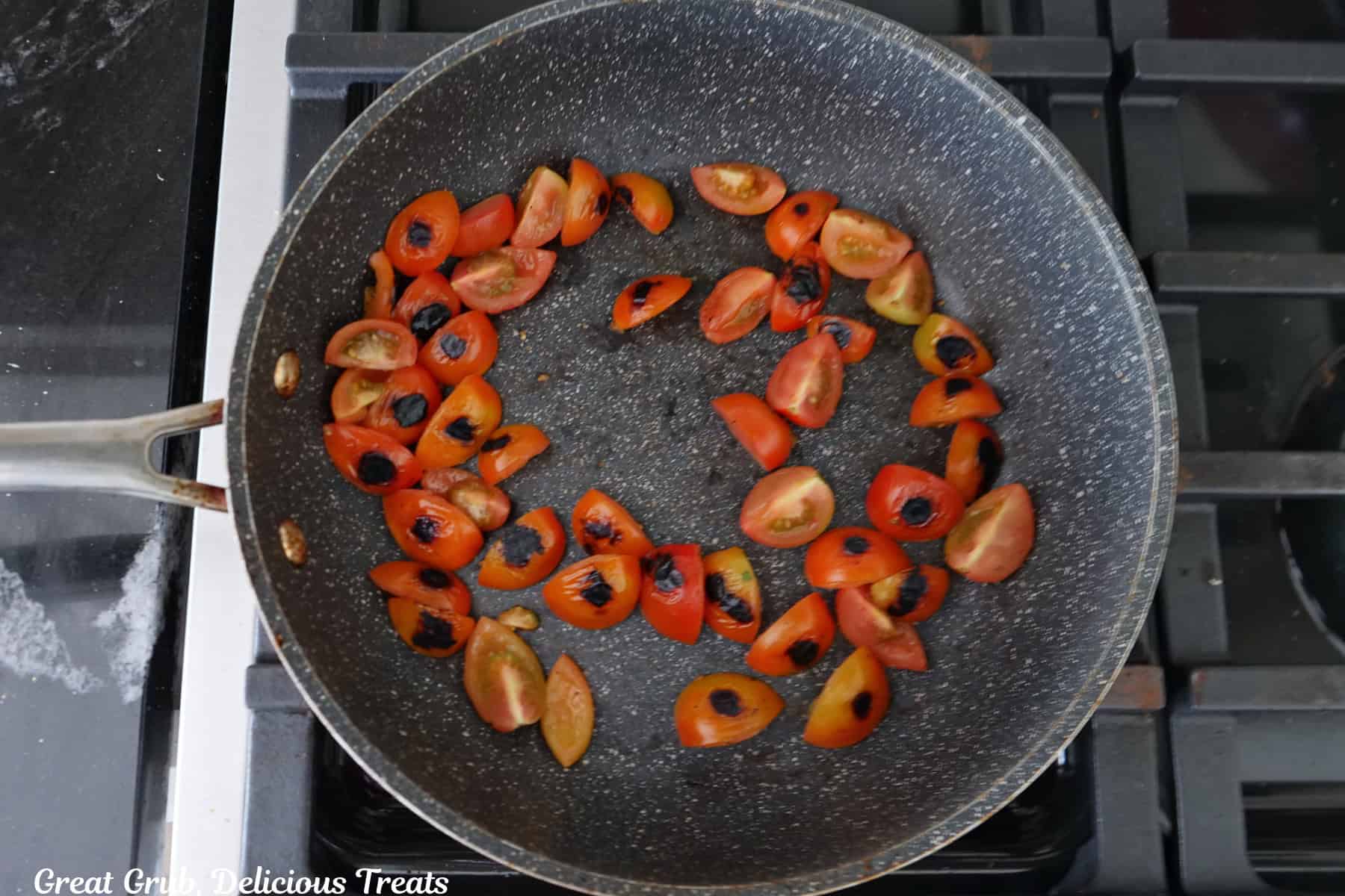 A frying pan with quartered cherry tomatoes in it being little charred on one side.