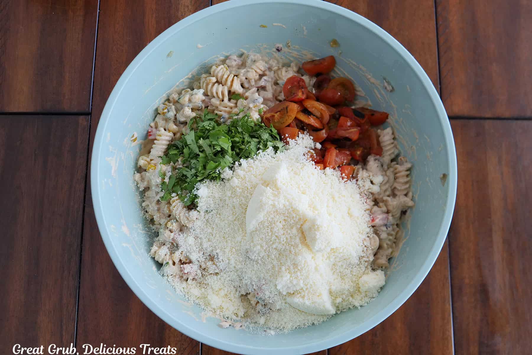 A wood surface with a light blue bowl filled with all the ingredients needed to make street corn pasta salad in it before being mixed together.