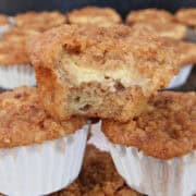 A stack of banana cream cheese muffins on top of each other with a bite taken out of the one on top, and a title overlay at the top.