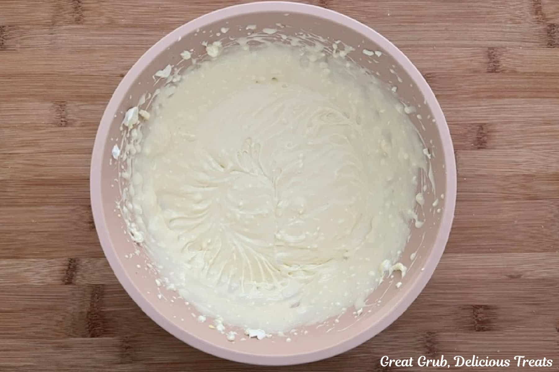 A wood surface with a mixing bowl filled with a cream cheese filling in it.