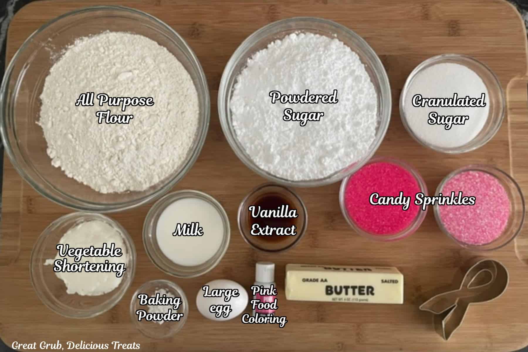 A wood surface with all the ingredients placed on it to make Breast Cancer Awareness Ribbon Sugar Cookies.