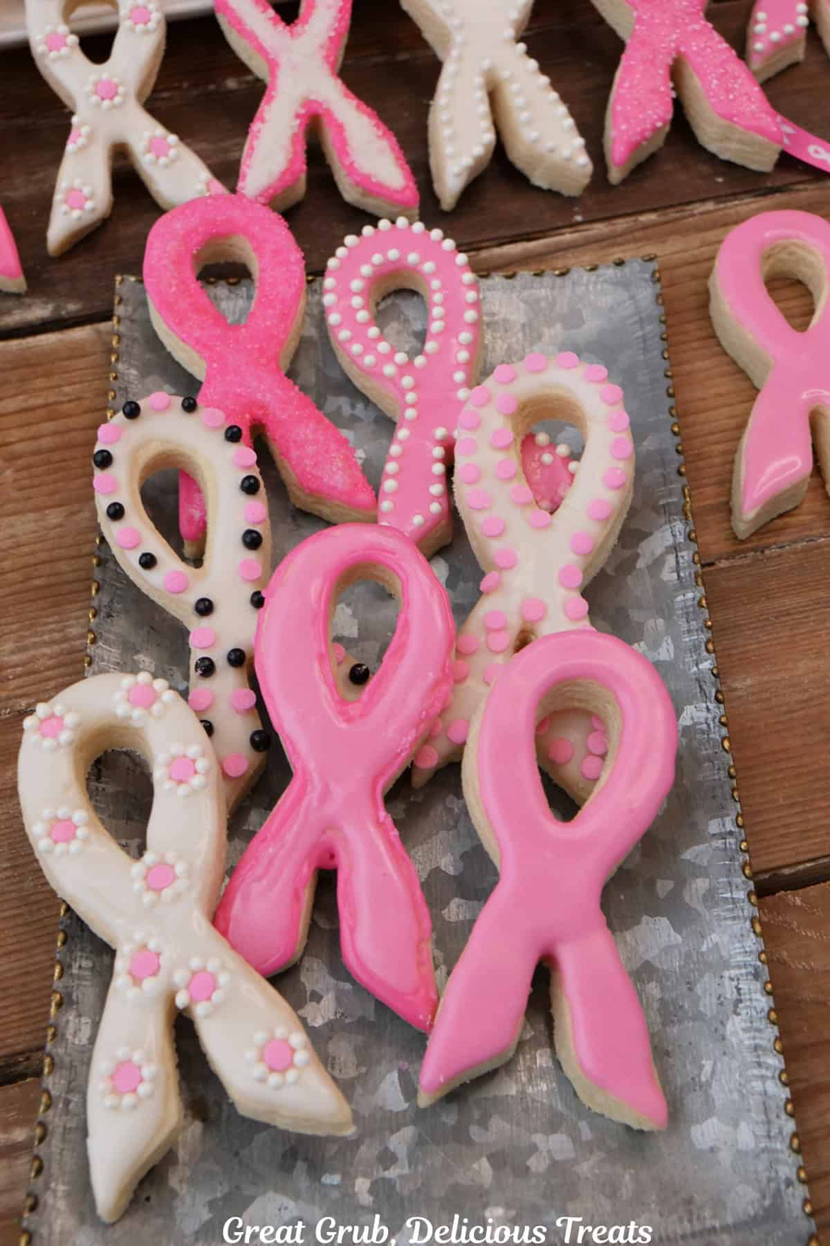 A silver tray with seven iced breasts cancer awareness ribbon sugar cookies on it with more in the background.