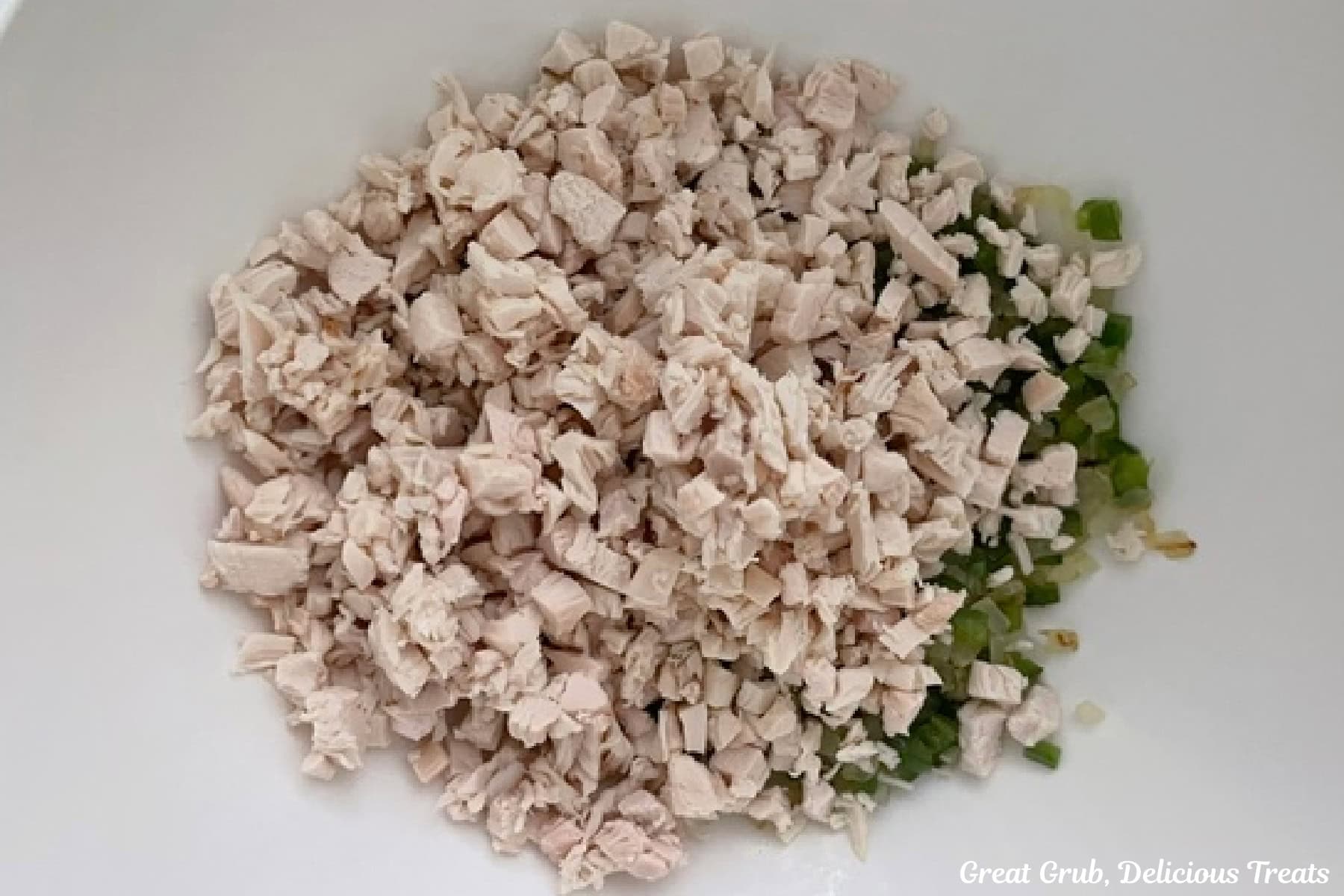 A white bowl with diced rotisserie chicken and cooked jalapenos and onions.