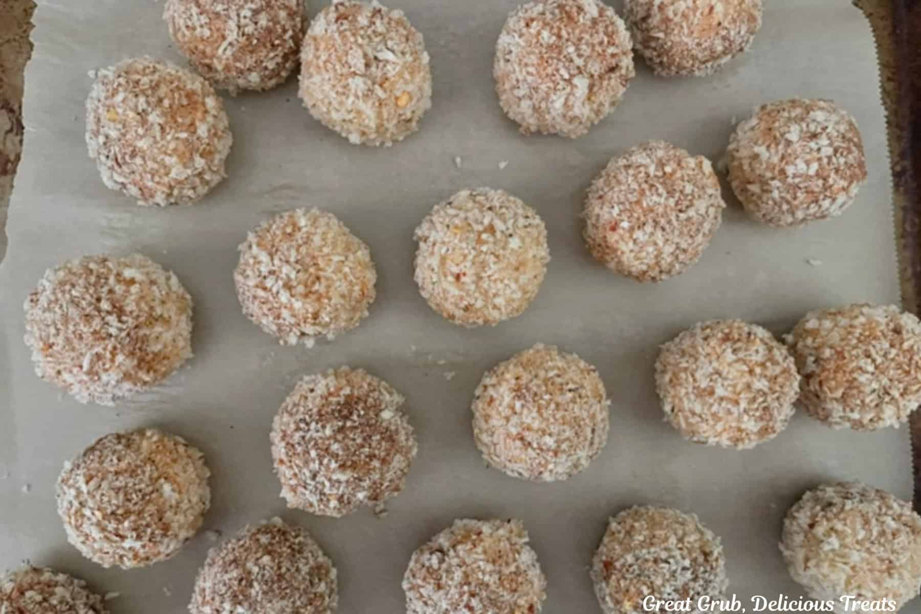 A baking sheet with twenty chicken rice bites coated in seasoned breadcrumbs placed on it.