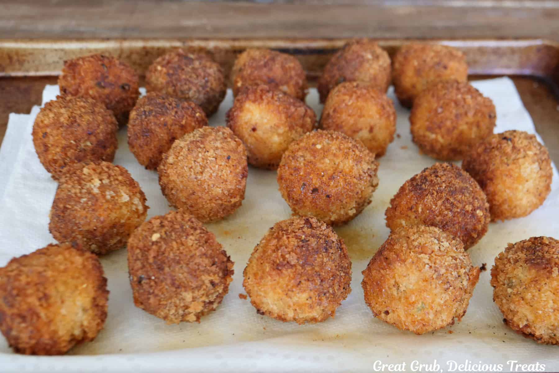 A baking sheet with deep fried cheesy chicken rice bites on it after being deep fried.