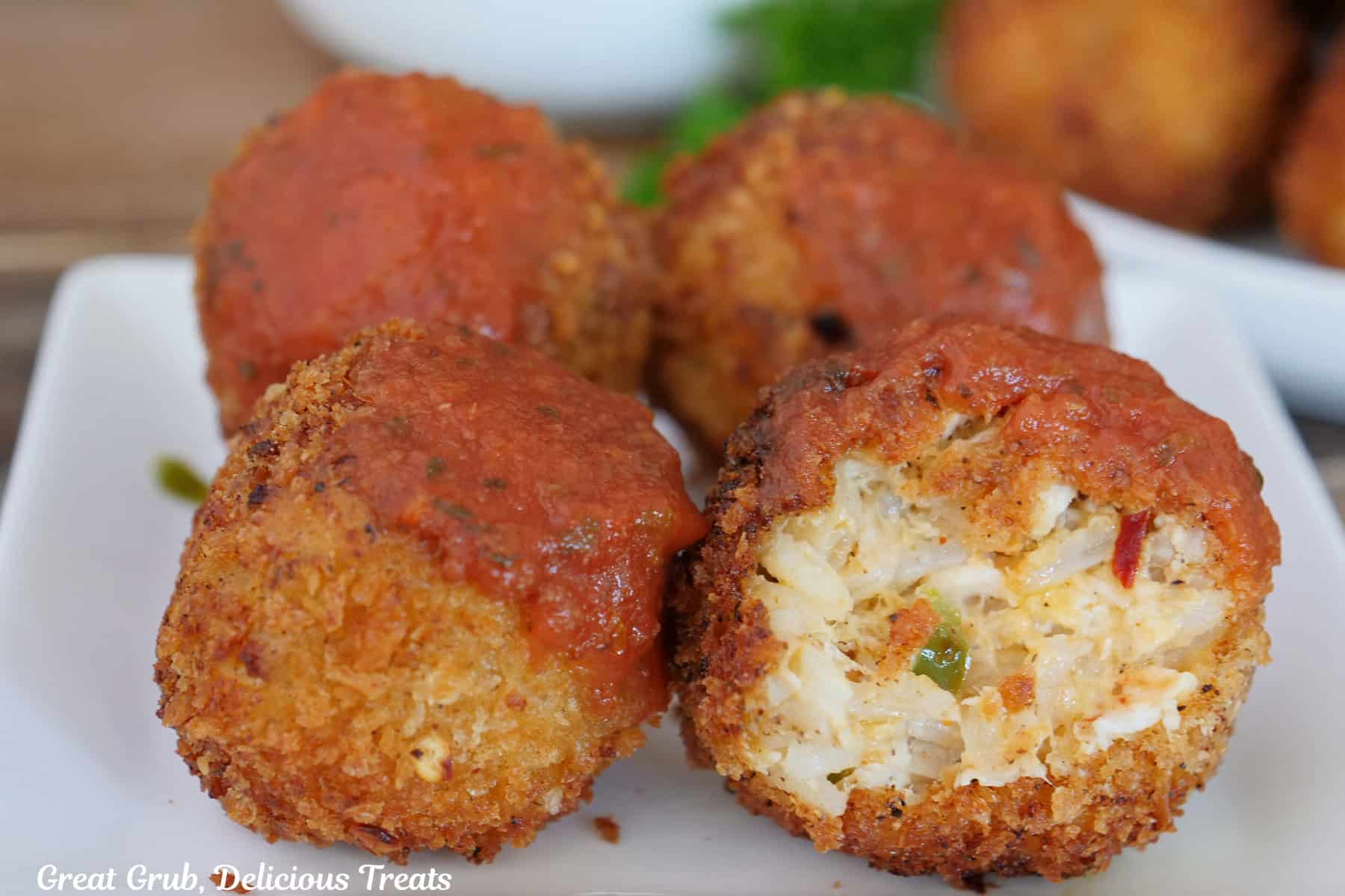 A white plate with four deep fried cheesy chicken rice bites on it with a bite taken out of the one in front.