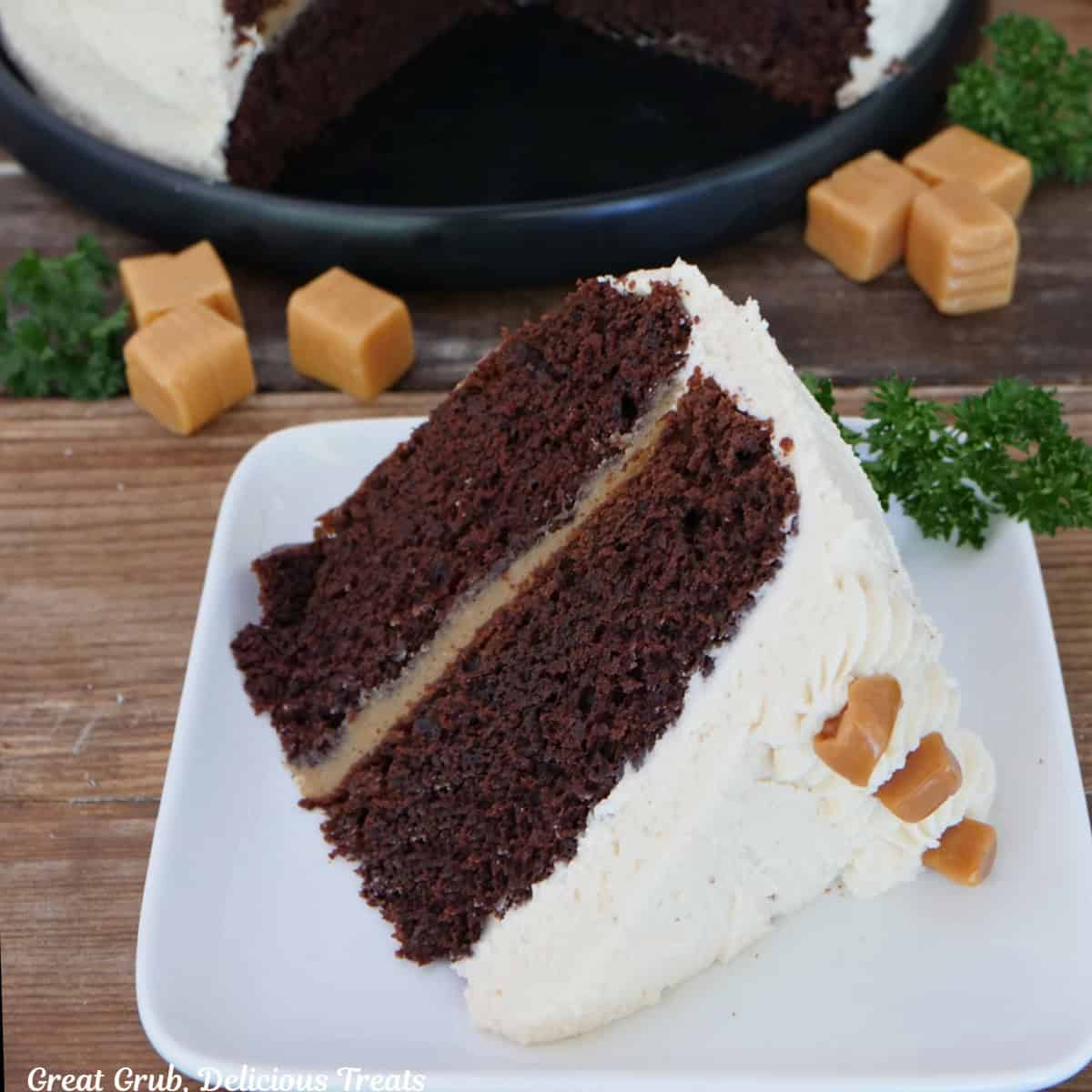 A two layer chocolate espresso cake with salted caramel buttercream frosting on a white square plate with a few pieces of caramel randomly placed around the plate.