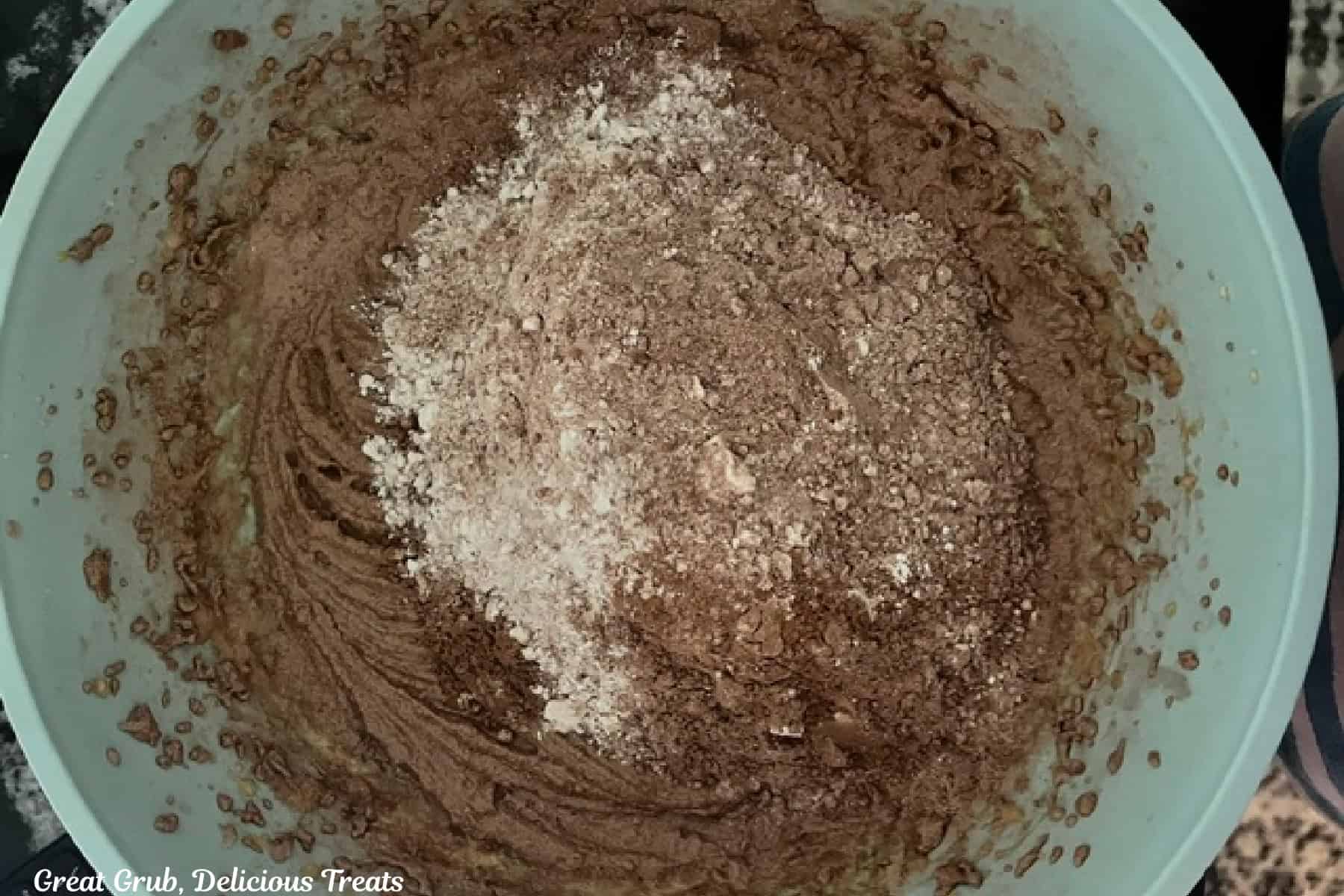 A light blue bowl with wet ingredients being mixed with dry ingredients for the chocolate cake.