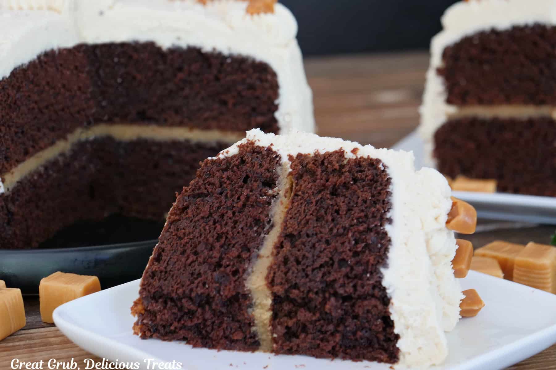 A slice of two layer chocolate espresso cake on a square white plate with another slice and the cake in the background.