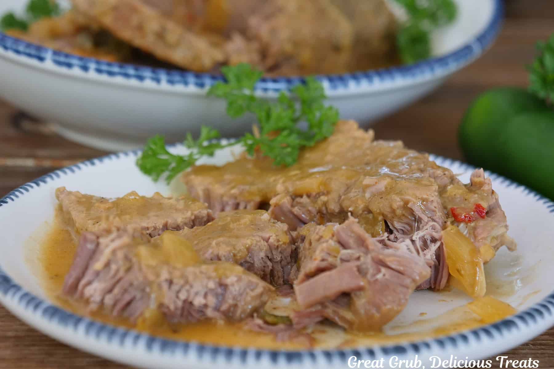 A round white plate with blue trim with a slice of slow cooked roast beef that has been cut into bite-size pieces with another plate in the background.