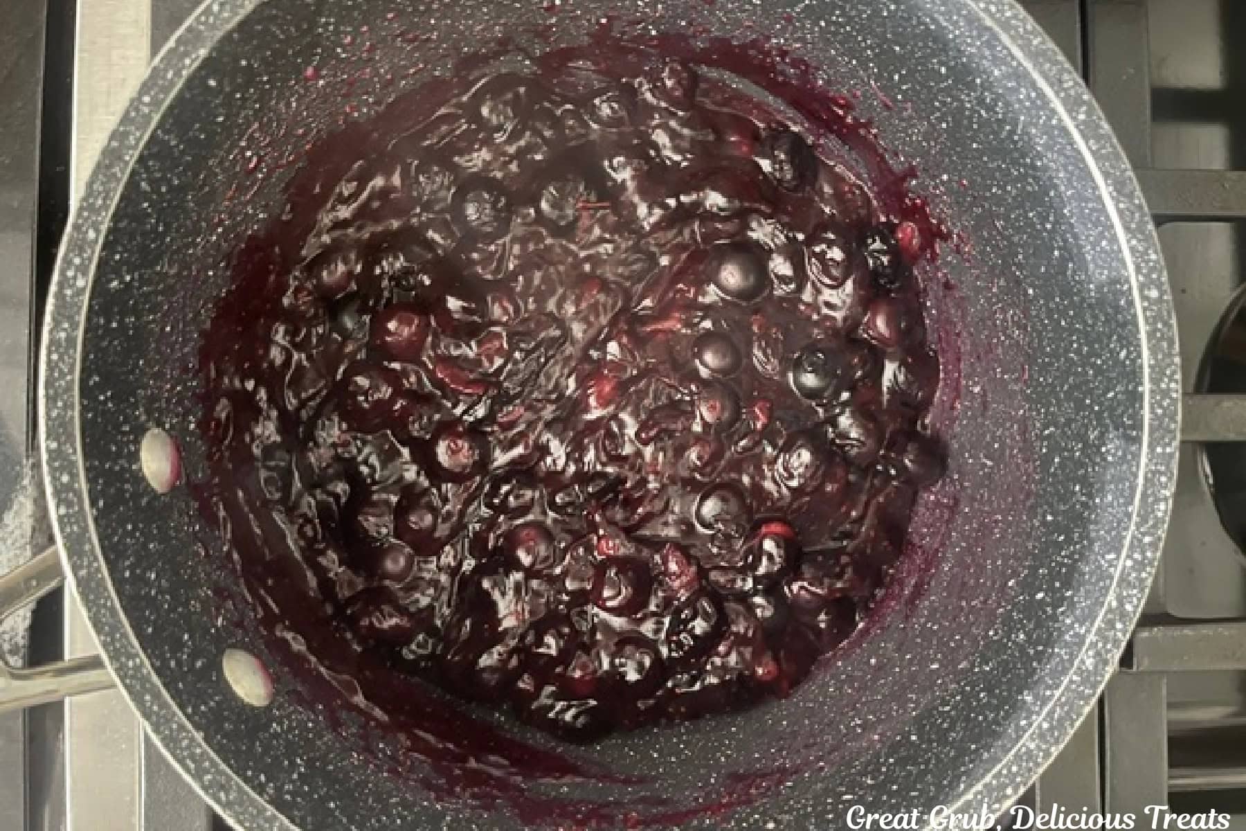 A saucepan with blueberry sauce in it cooking on the stove.