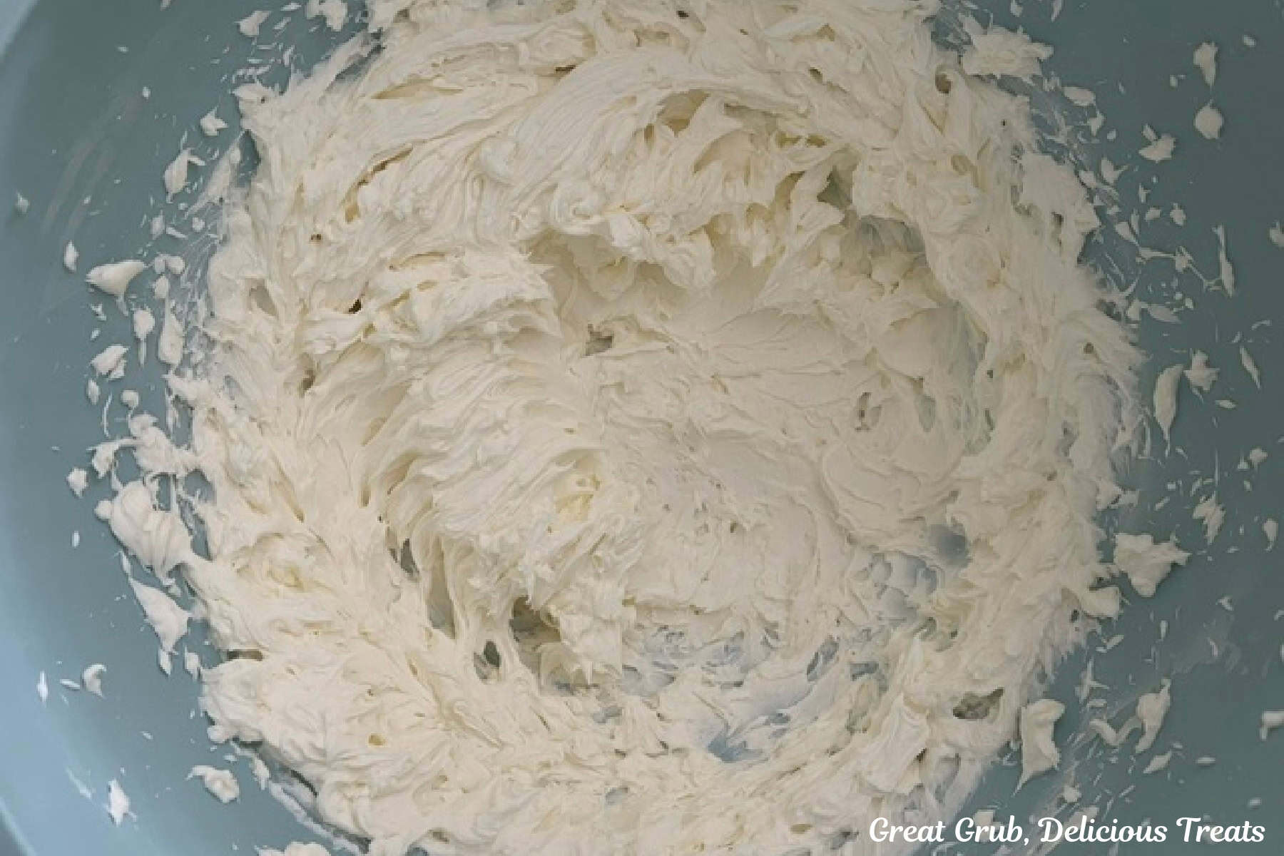 A light blue bowl with cream cheese that has been beaten until smooth.