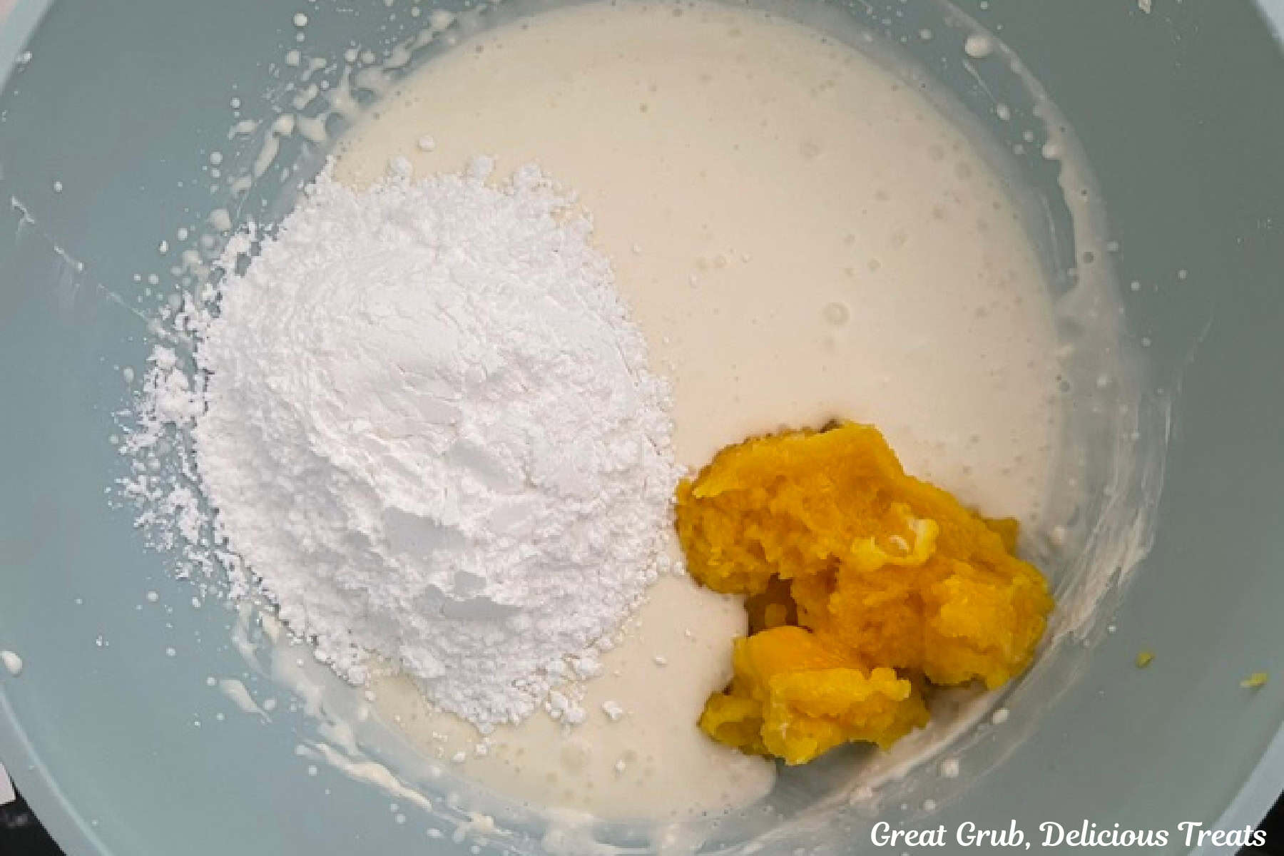 A light blue bowl with cream cheese mixture, powdered sugar, and thick lemon pudding mixture before being mixed together.