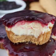 Two mini peanut butter and jelly cheesecakes stacked on top of each other with a bite taken out of the one on top, and a title overlay at the top.