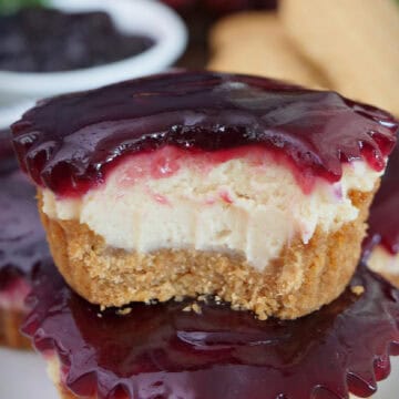 Two mini peanut butter and jelly cheesecakes stacked on top of each other with a bite taken out of the one on top, and a title overlay at the top.