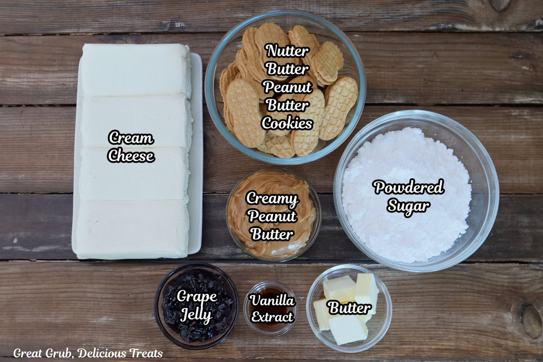 A rustic wood surface with all the ingredients placed on it to make mini peanut butter and jelly cheesecakes.