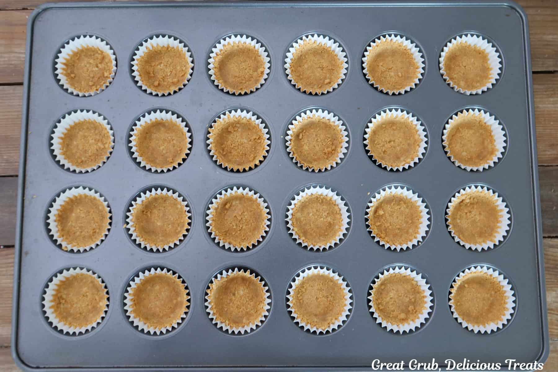 A mini 24-count muffin tin with cookie crusts in it before being baked.