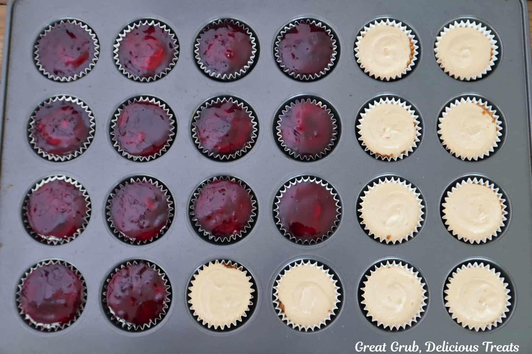 A 24-count mini muffin tin with grape jelly being added to the top of the mini peanut butter cheesecakes.
