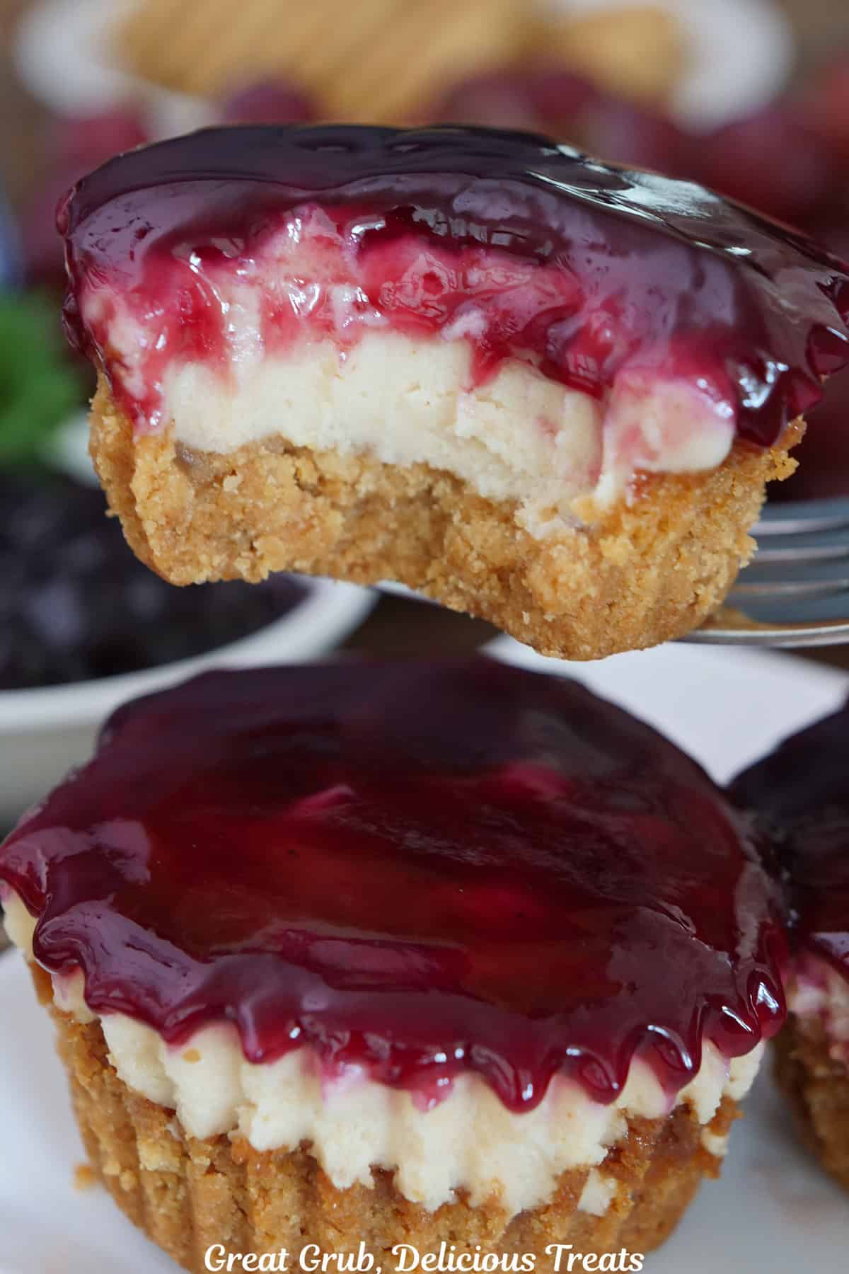 Two mini peanut butter and jelly cheesecakes with one held above the other with a bite taken out of it.