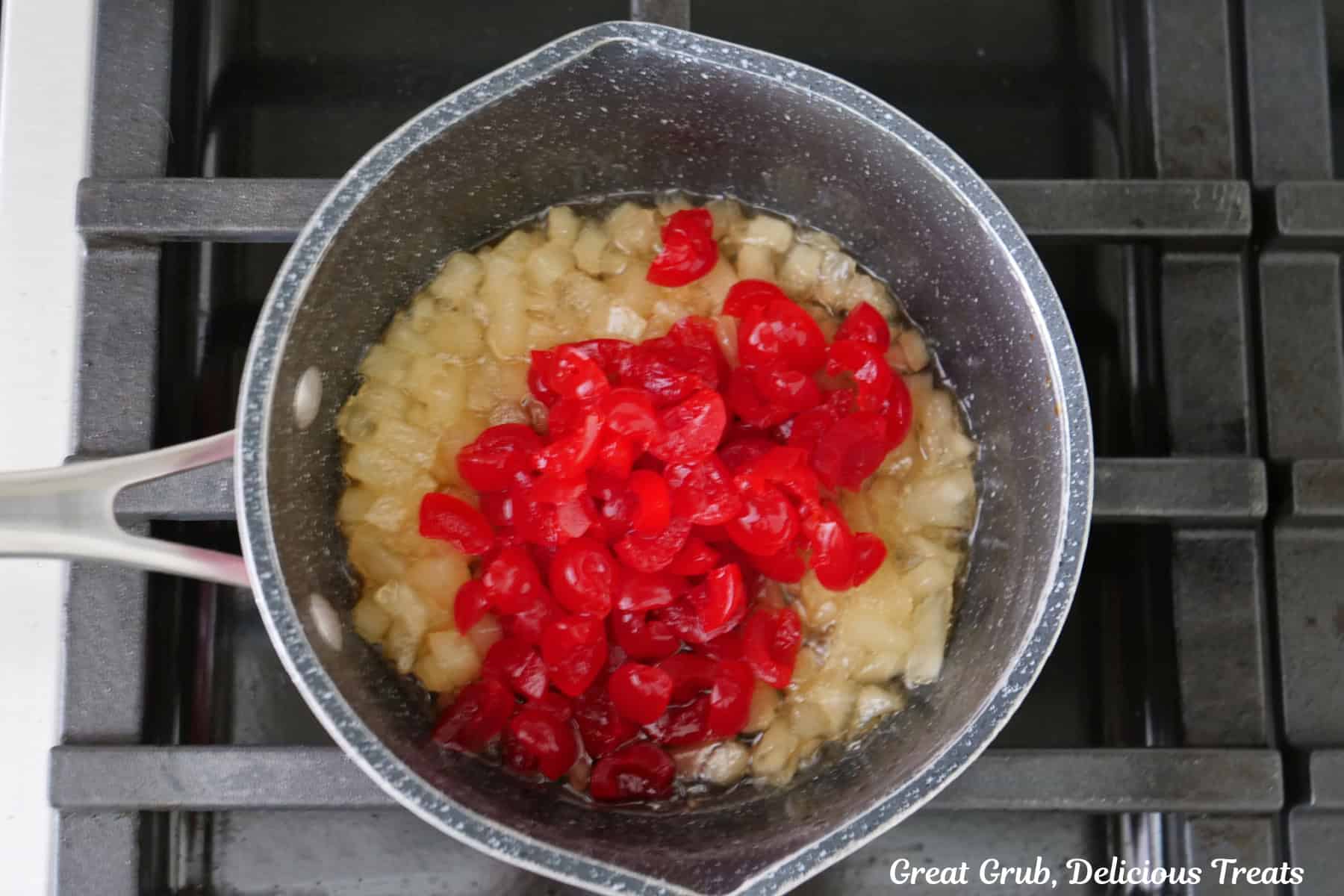 A saucepan with chopped pineapple and cherries on the stove.