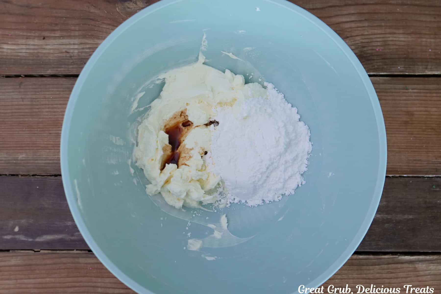 A wood surface with a light blue bowl filled with the cheesecake ingredients before being mixed together.
