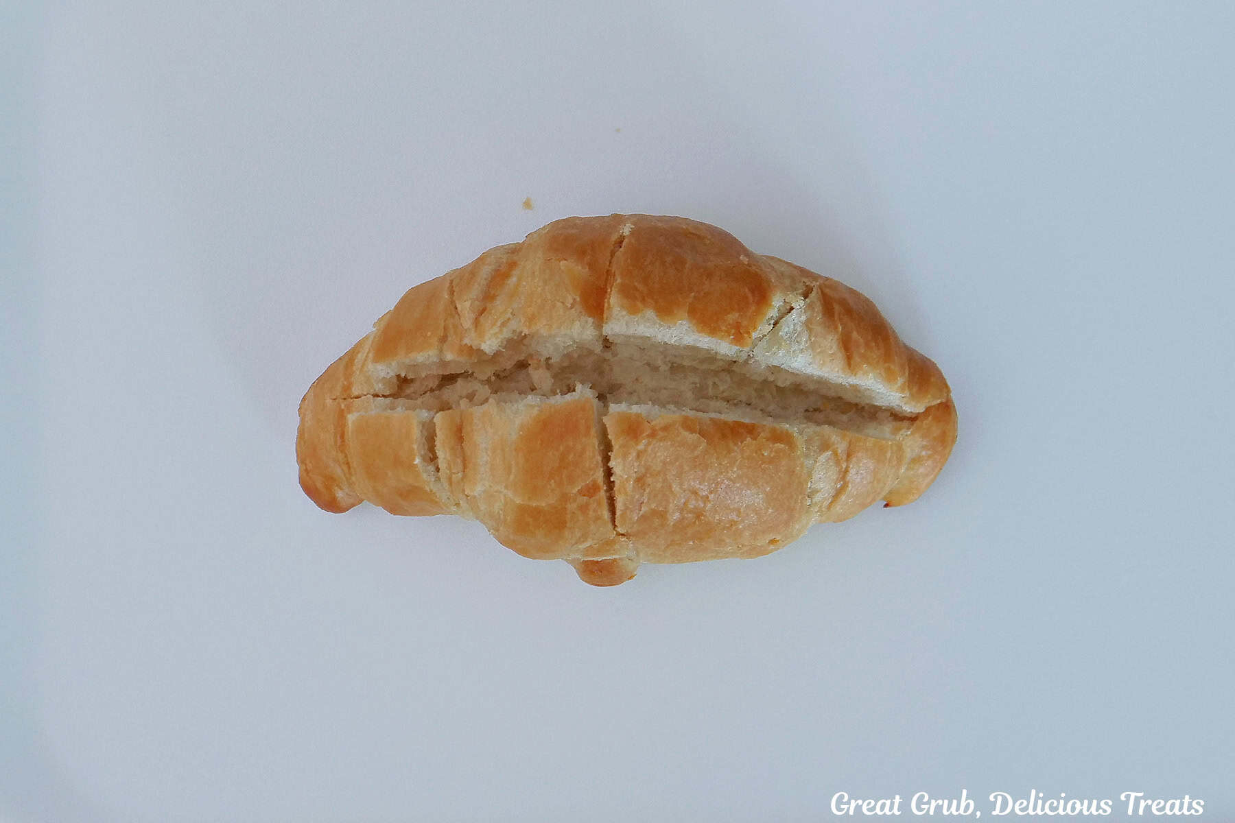 A white surface with a mini croissant on it showing how to make the cuts in the top to add the cheesecake ingredients.
