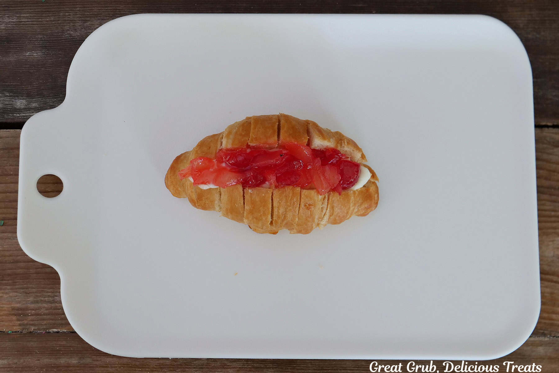 A white surface with a mini croissant on it filled with the cheesecake pineapple cherry filling.