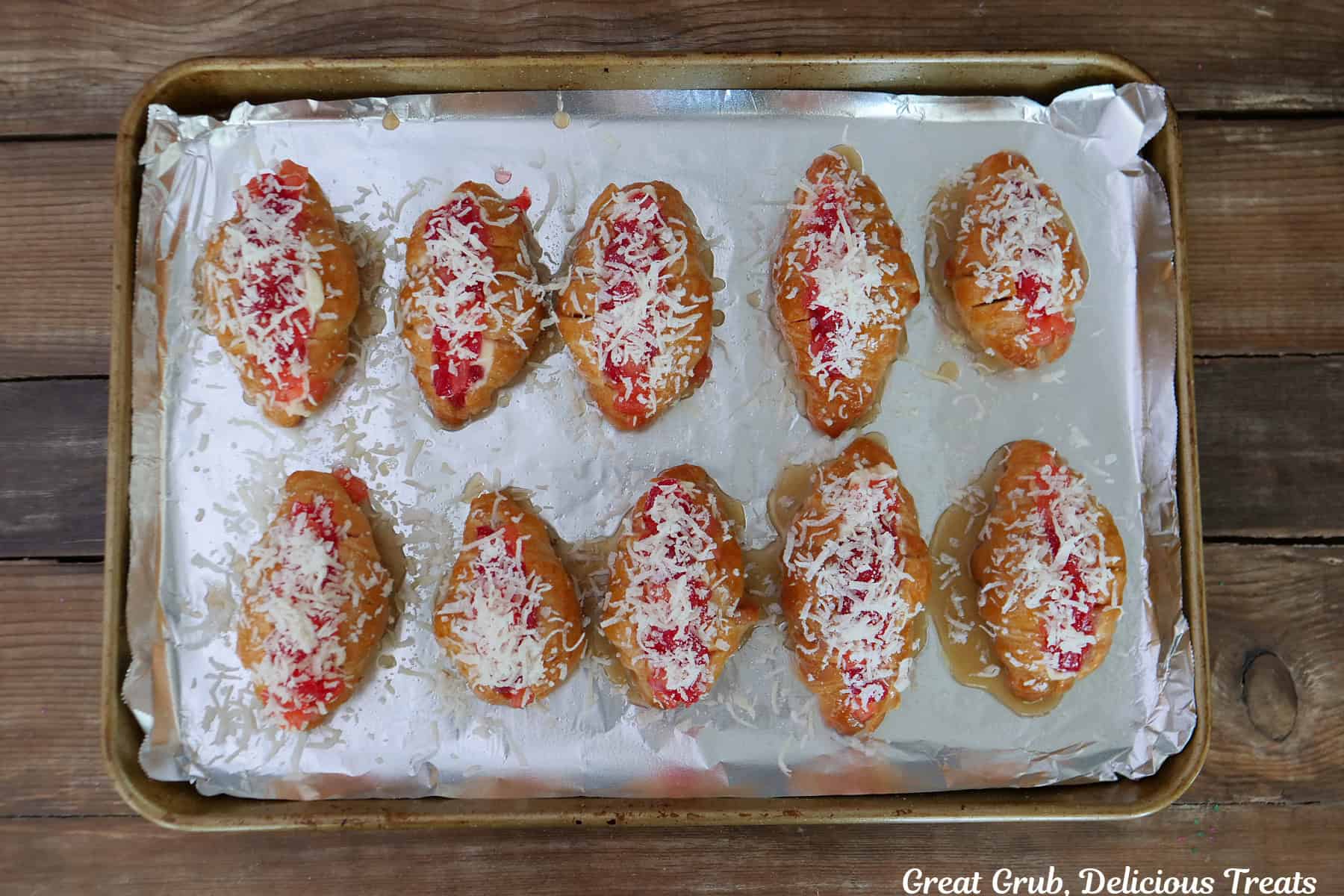 A foil lined baking sheet with ten mini pineapple cherry cheesecake croissants on it before going into the oven.
