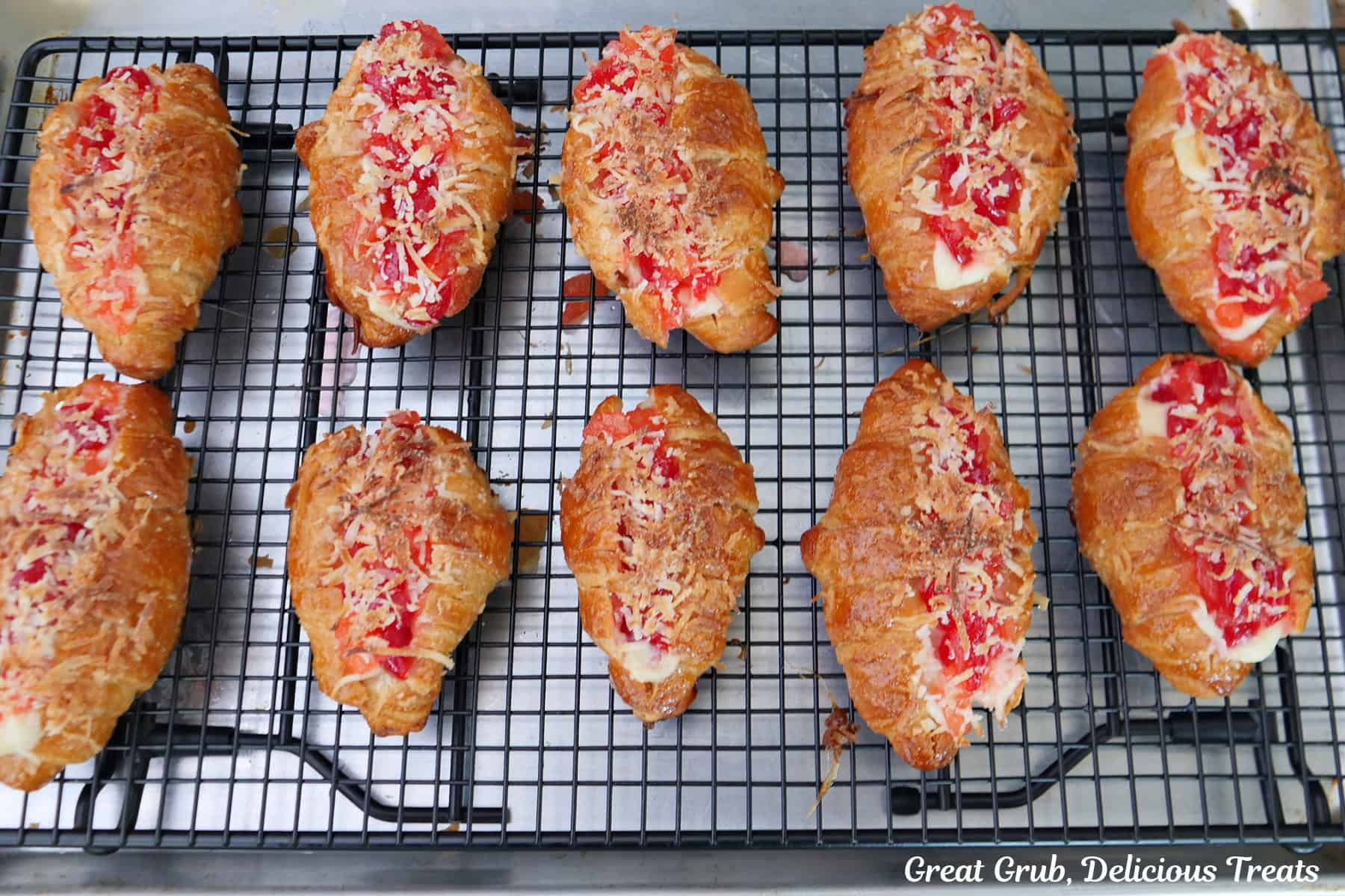 A foil lined baking sheet with a wire rack on top with ten baked mini pineapple cherry cheesecake croissants on it.