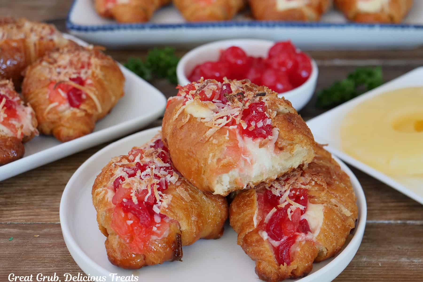 A wood surface with mini pineapple cherry cheesecake croissants on it with more in the background.