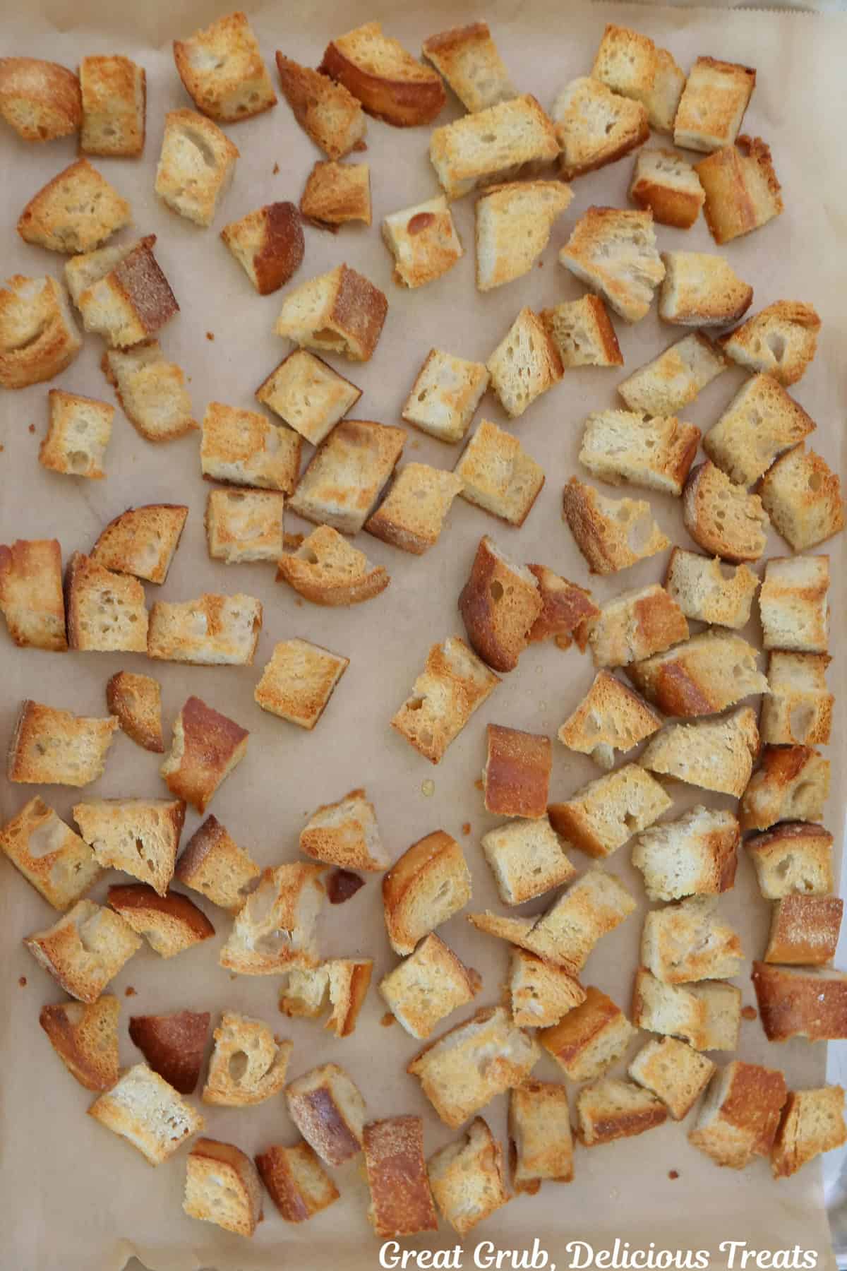 A parchment lined baking sheet with crusty one inch pieces of bread on it.