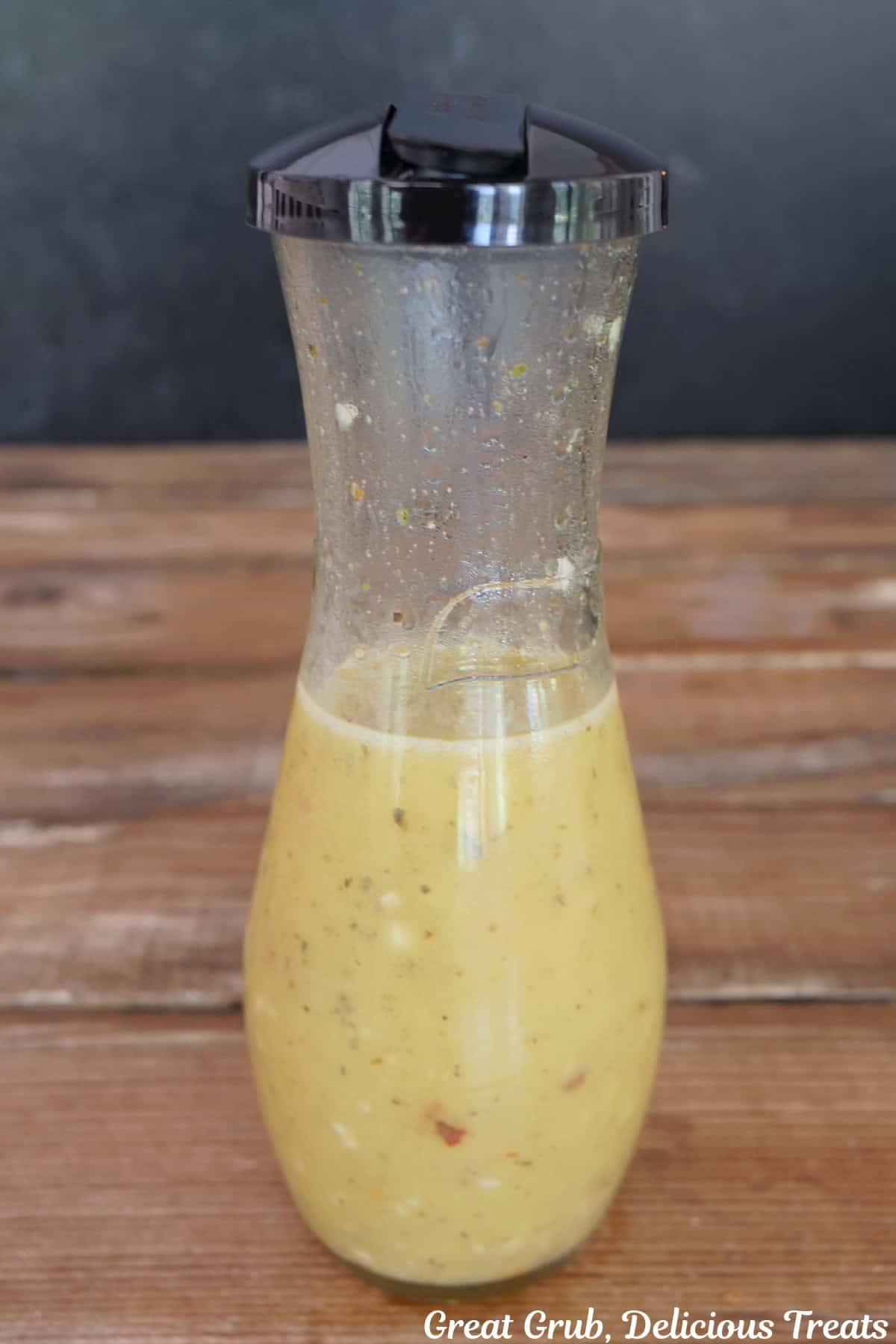 A rustic wood surface with a shaker bottle filled with lemon vinaigrette dressing in it.