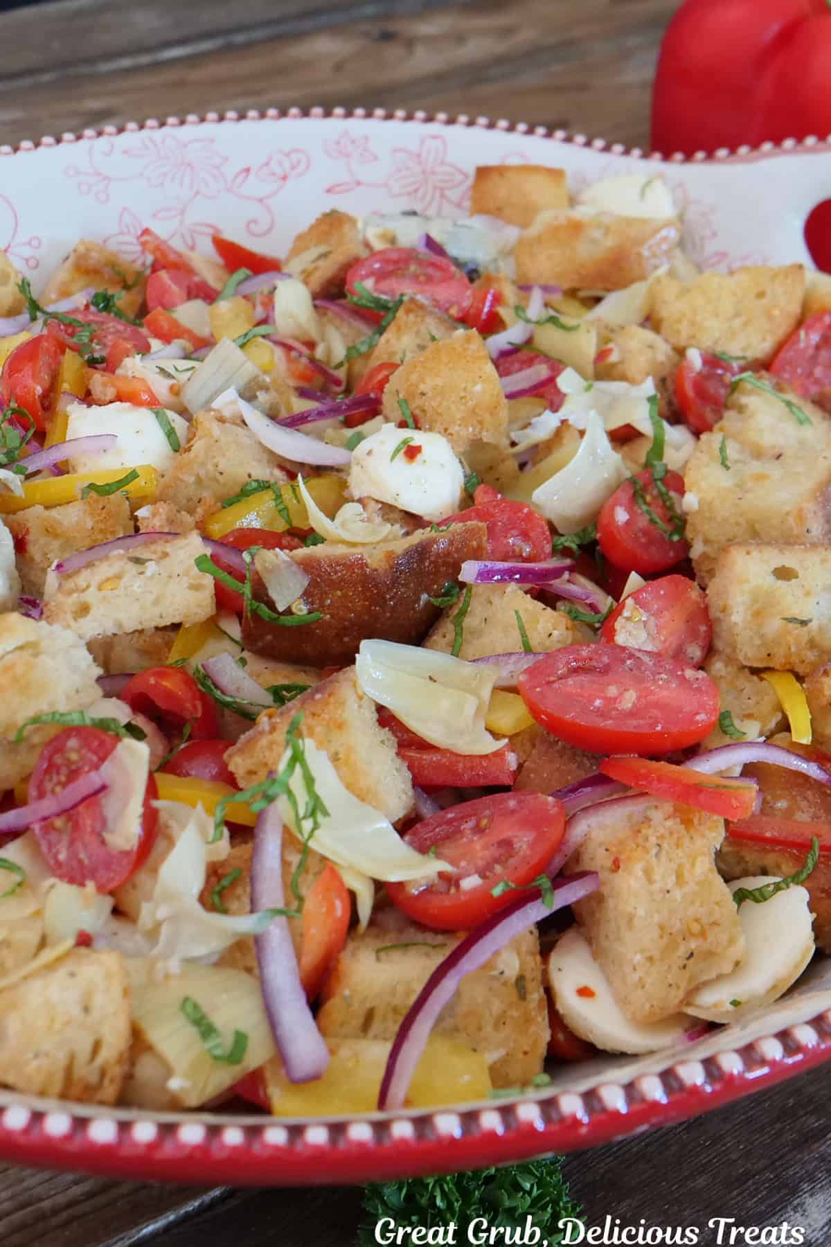 A large red and white bowl filled with panzanella salad.