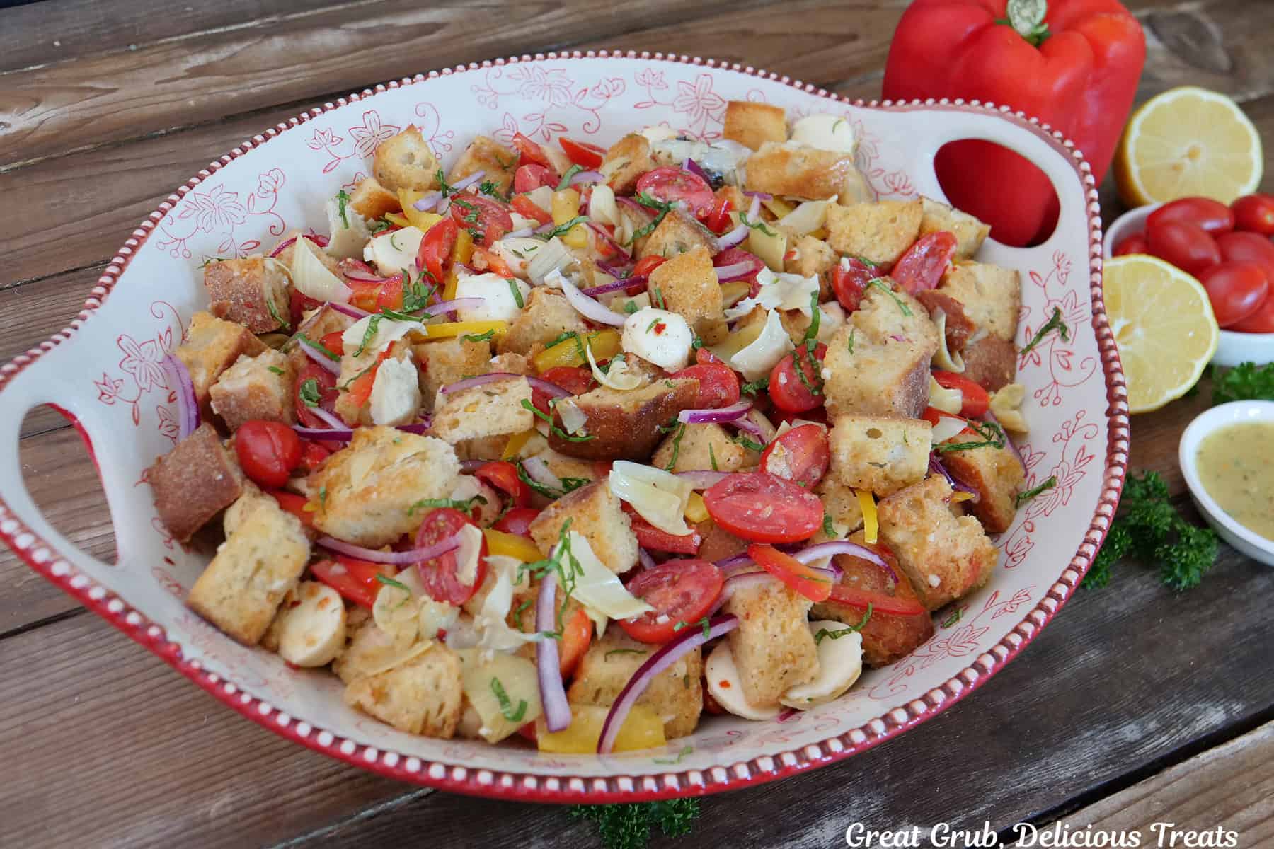 A wood surface with a red and white bowl filled with panzanella salad.