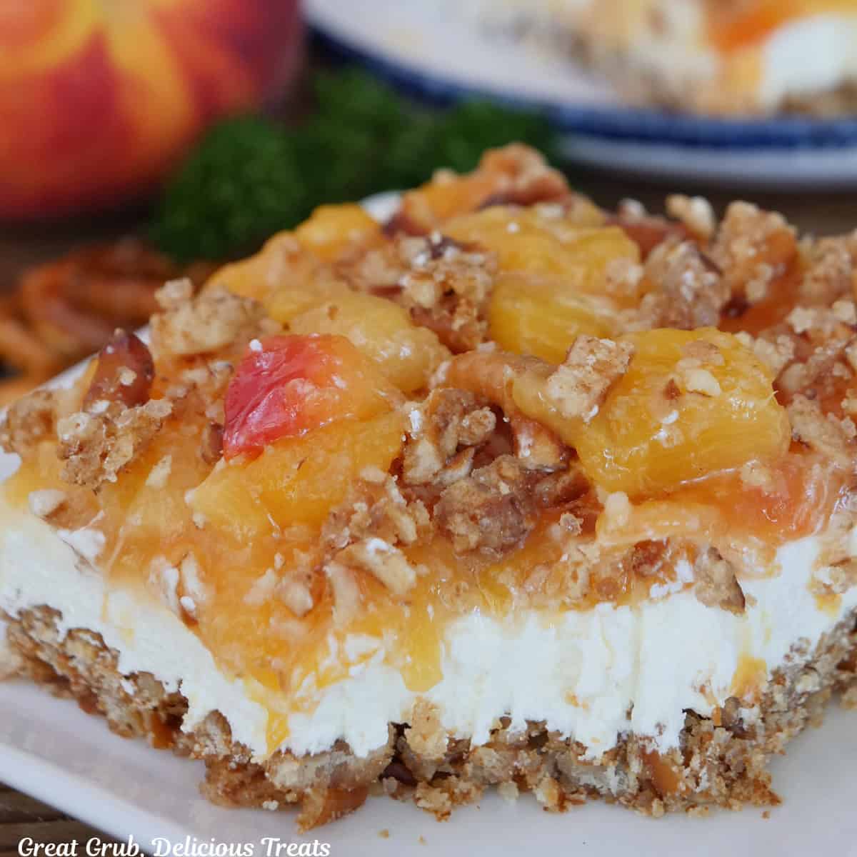 A white square plate with a serving of peach pretzel dessert with a bite taken out of it.