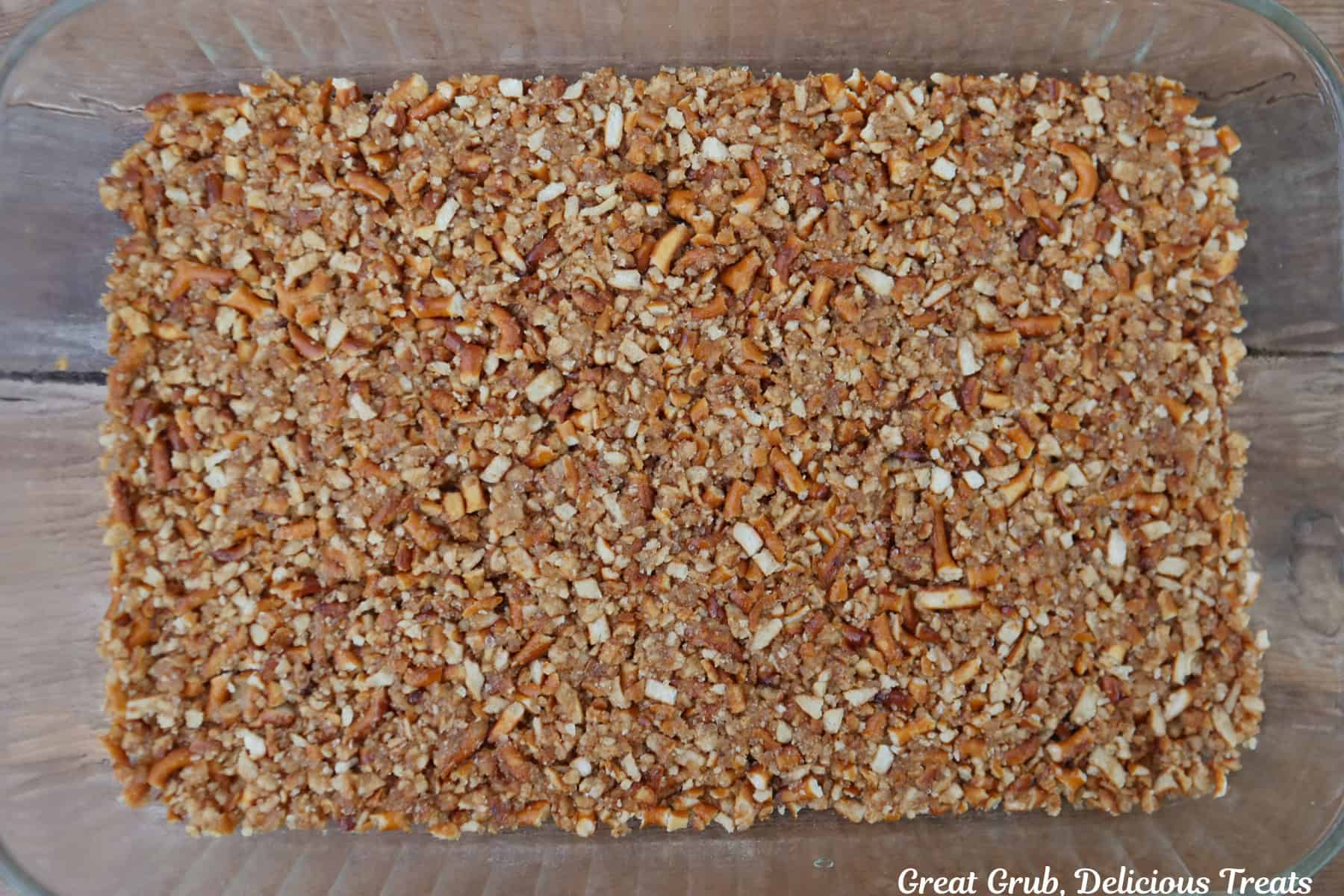 A wood surface with a glass 9 by 13 baking dish with a pretzel crust in it.