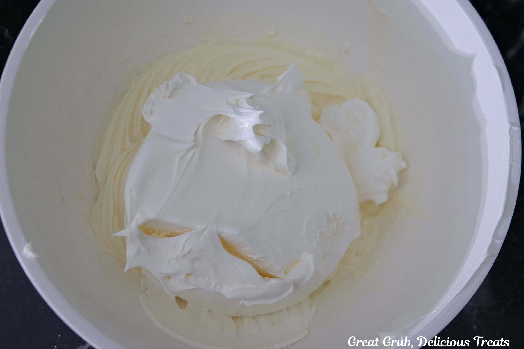 A white bowl with cream cheese, powdered sugar, and cool whip before being combined together.