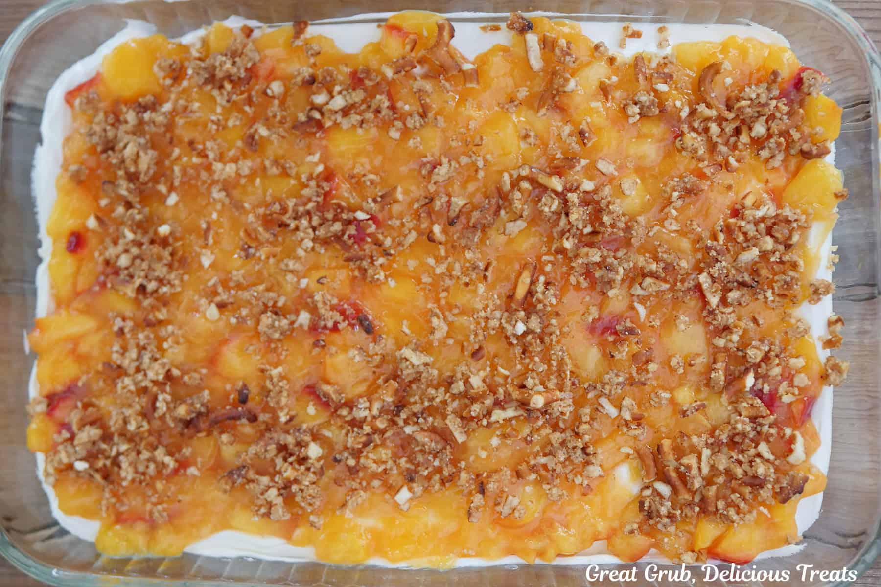 A glass 9 by 13 baking dish with peach pretzel dessert in it.