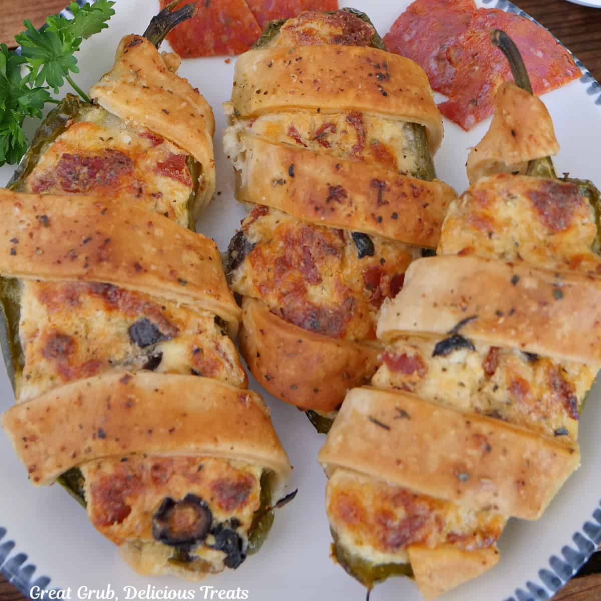 A white round plate with blue trim with three pepperoni pizza jalapeno poppers on it.