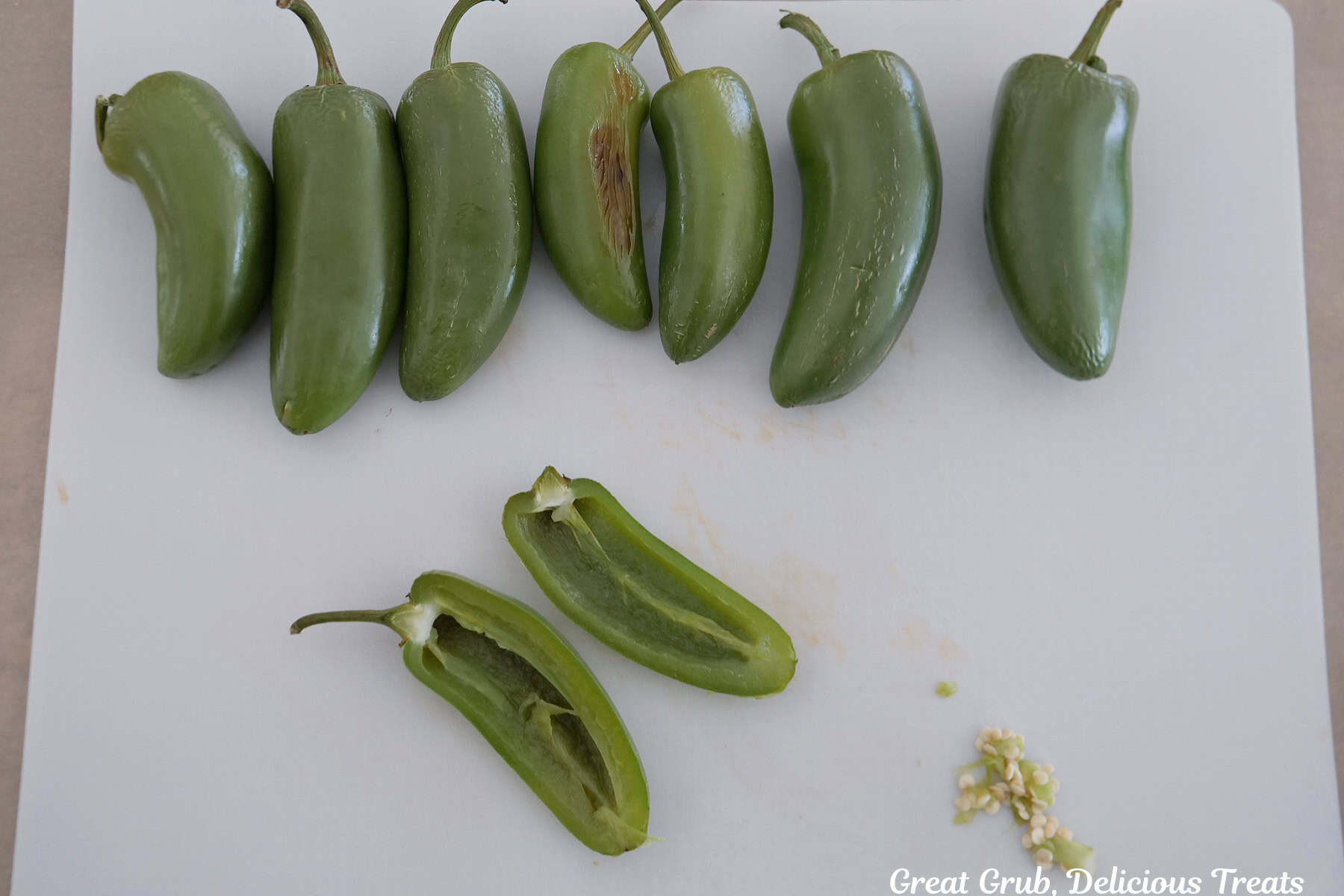 Eight roasted jalapenos on a piece of parchment paper and one pepper cut in half with the seeds removed.