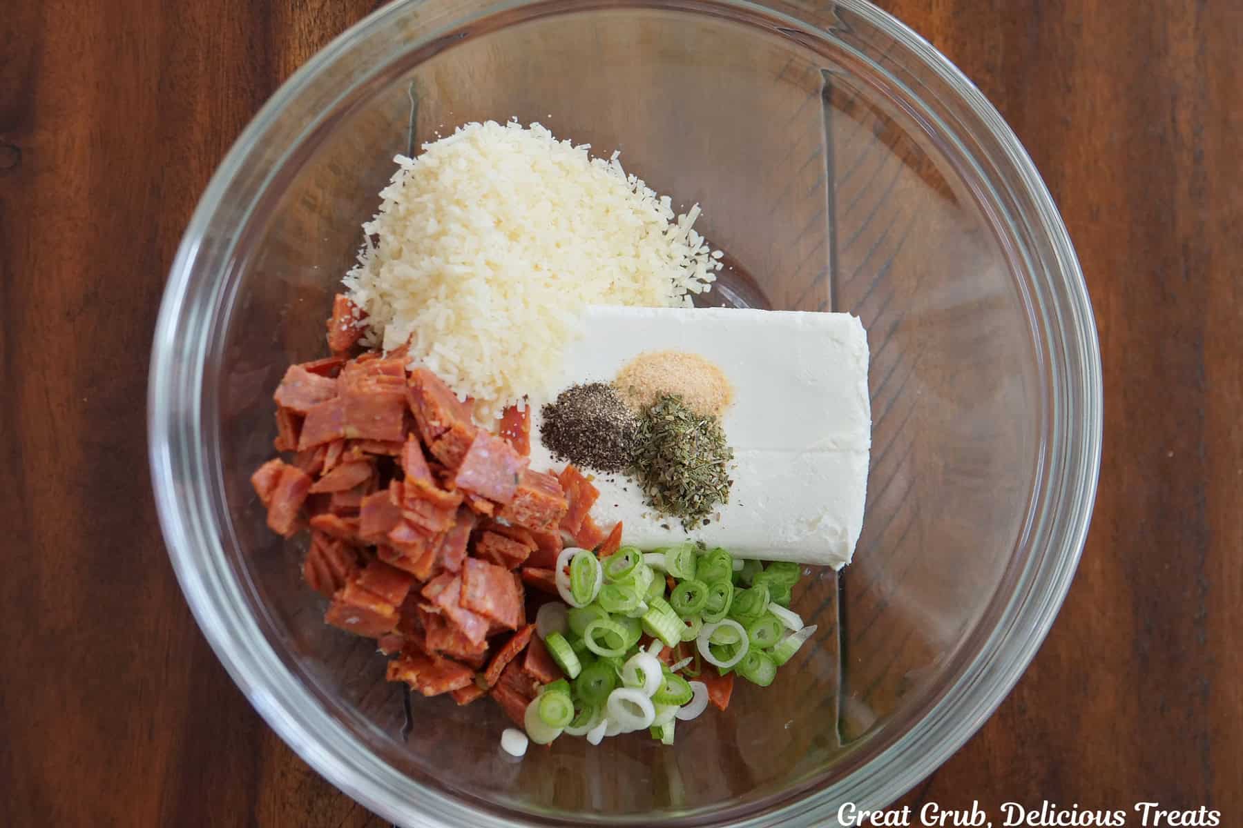 A wood surface with a glass bowl with some of the cream cheese pepperoni pizza mixture in it before being mixed together.