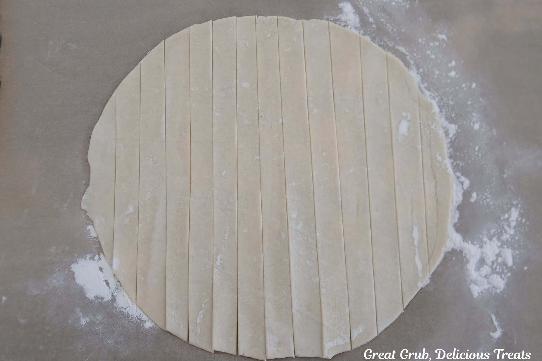 A round pie crust dough placed on a piece of parchment paper with ½ inch strips cut into the dough.