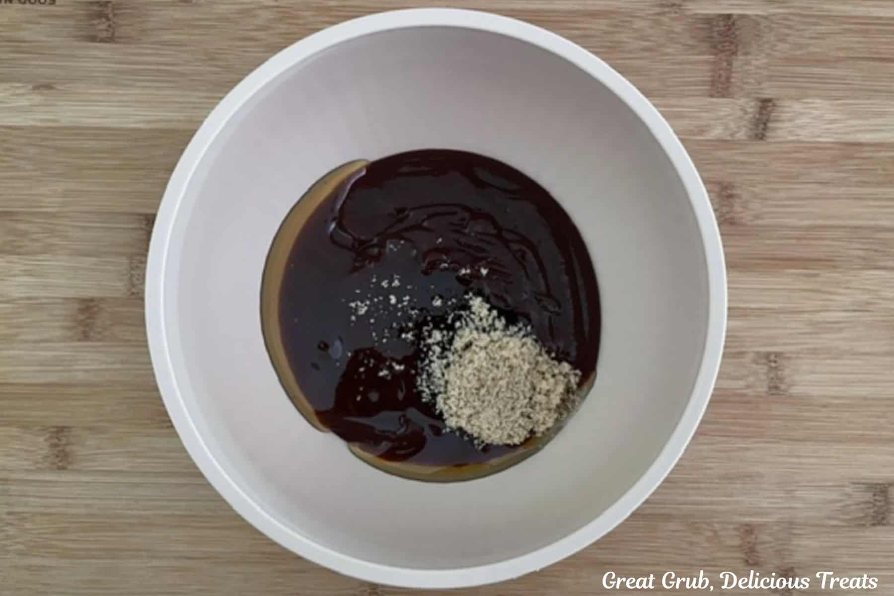 A wood surface with a white bowl filled with barbecue sauce, honey, and brown sugar before being mixed together.